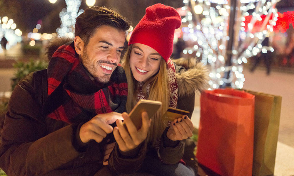 couple smiling outside on their phones during holidays