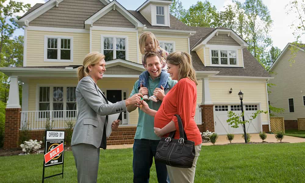 couple shaking hands with realtor outside of a new home