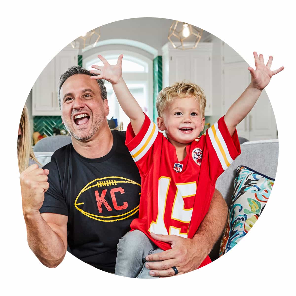 Father and young son celebrate a Kansas City Chiefs victory in their living room.