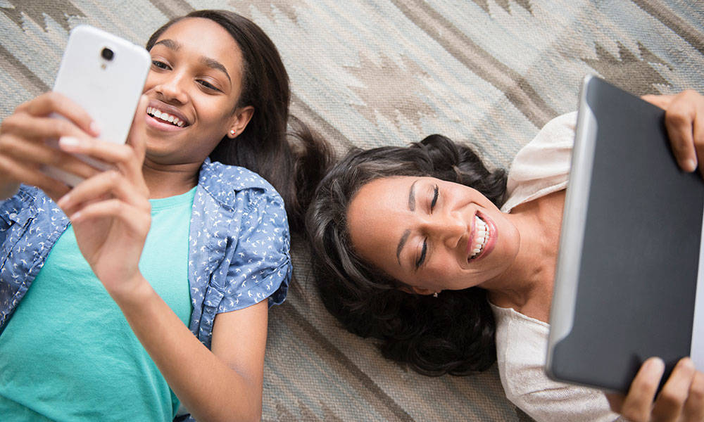 Mother and daughter laying on carpet using cell phone and tablet