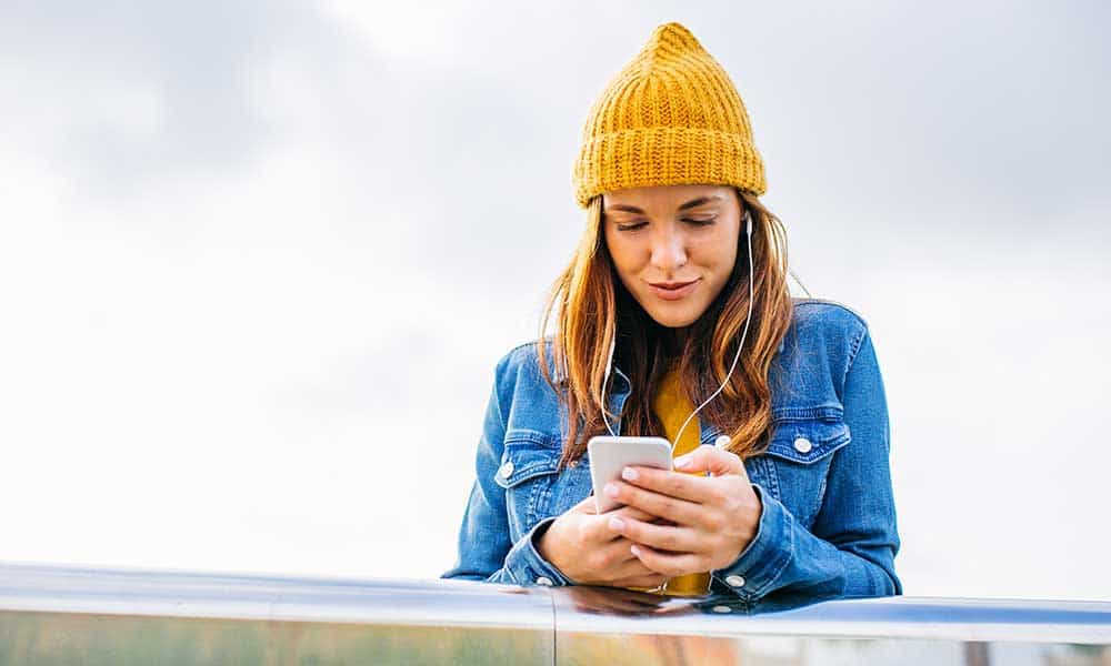 woman in yellow beanie cap looking at smartphone