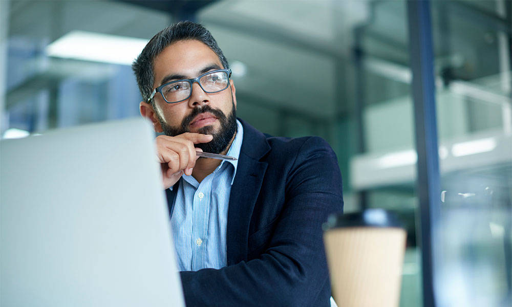 Mature businessman looking thoughtful while working on a laptop in an office.