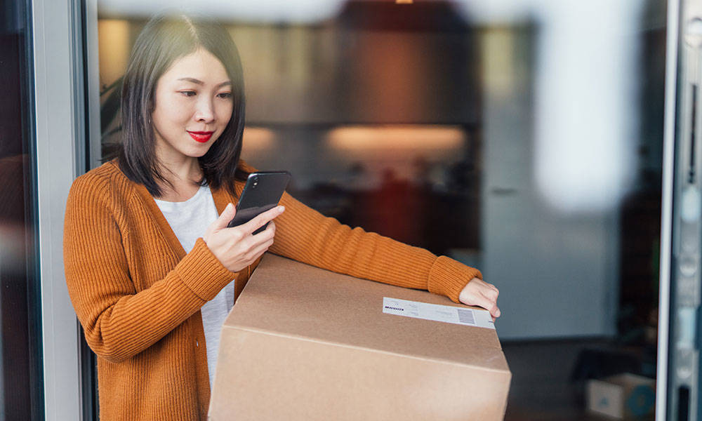 woman receiving package delivery and looking to smartphone for confirmation