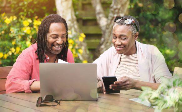 Smiling older couple using a laptop and smartphone outdoors.