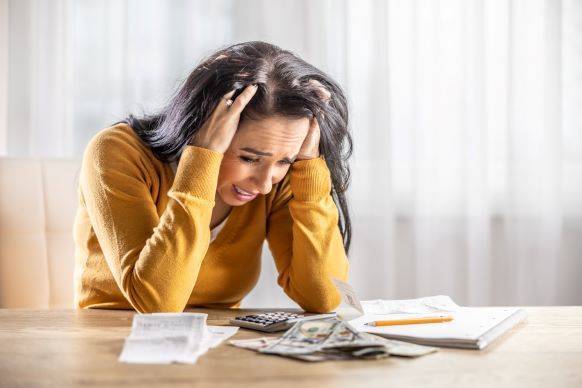 Woman stressed with hands in hair while reviewing financial documents at kitchen counter