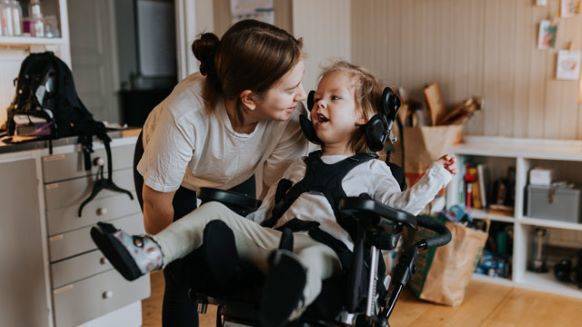 Mother talking and smiling with special needs daughter in wheel chair.