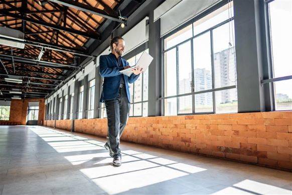 Man walking along windows of small business building working on laptop.